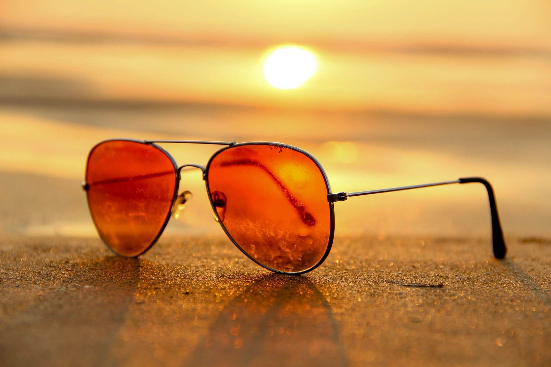 Sunglasses with orange lenses reflecting a sunset on the beach.