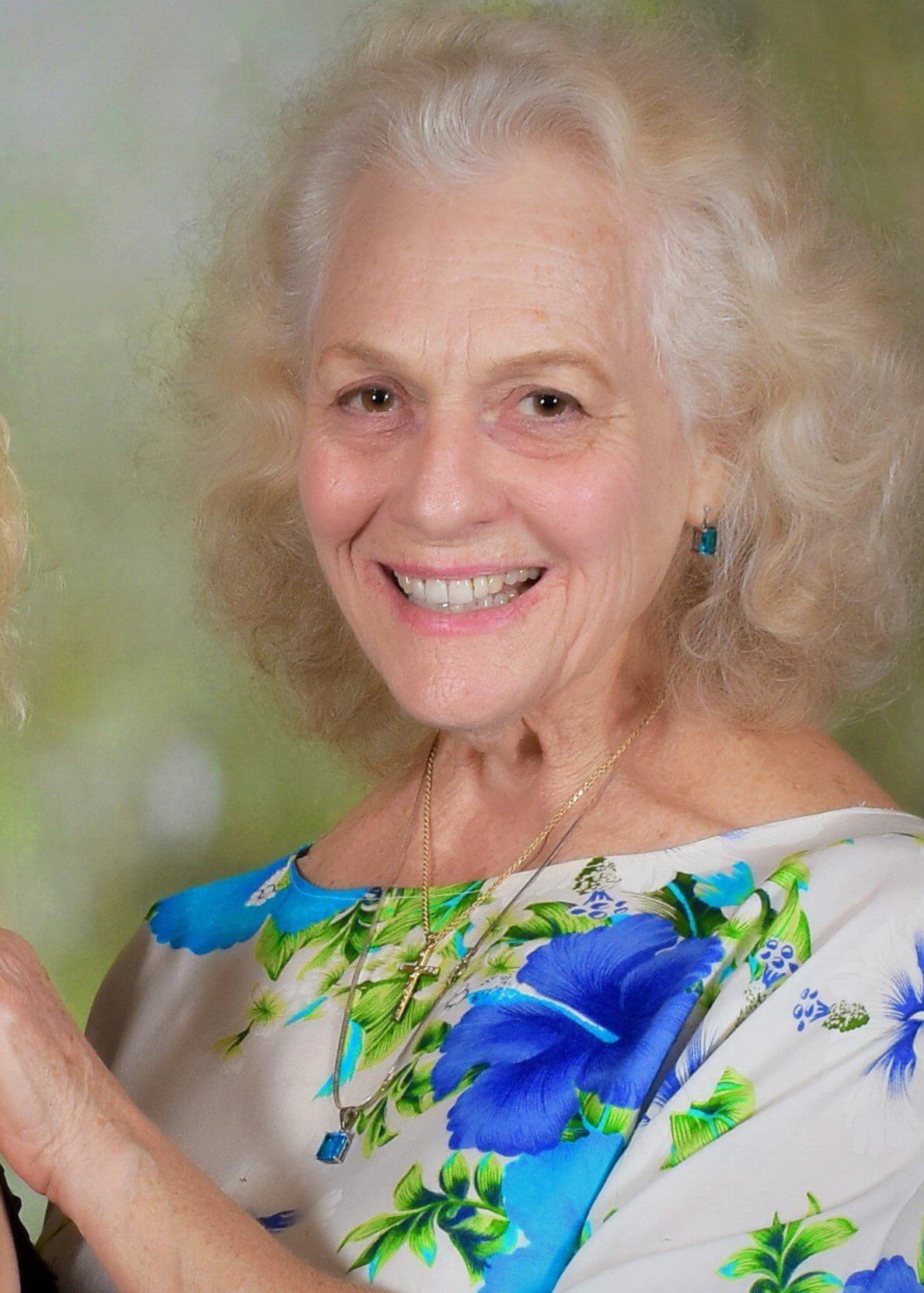 Smiling elderly woman in a floral dress with white hair.
